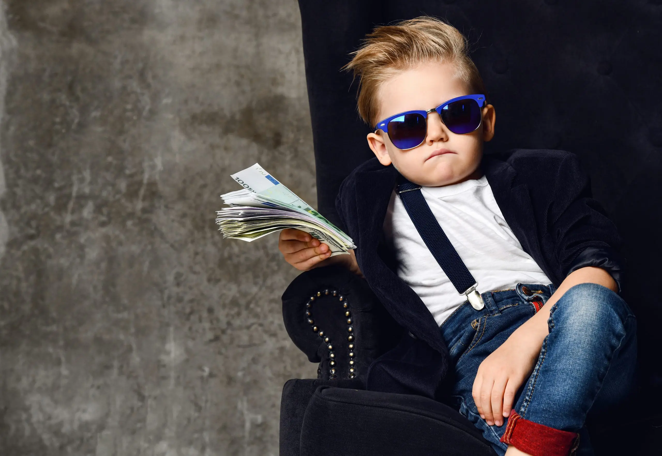 Happy and shoutting rich kid boy millionaire sits with a bundle