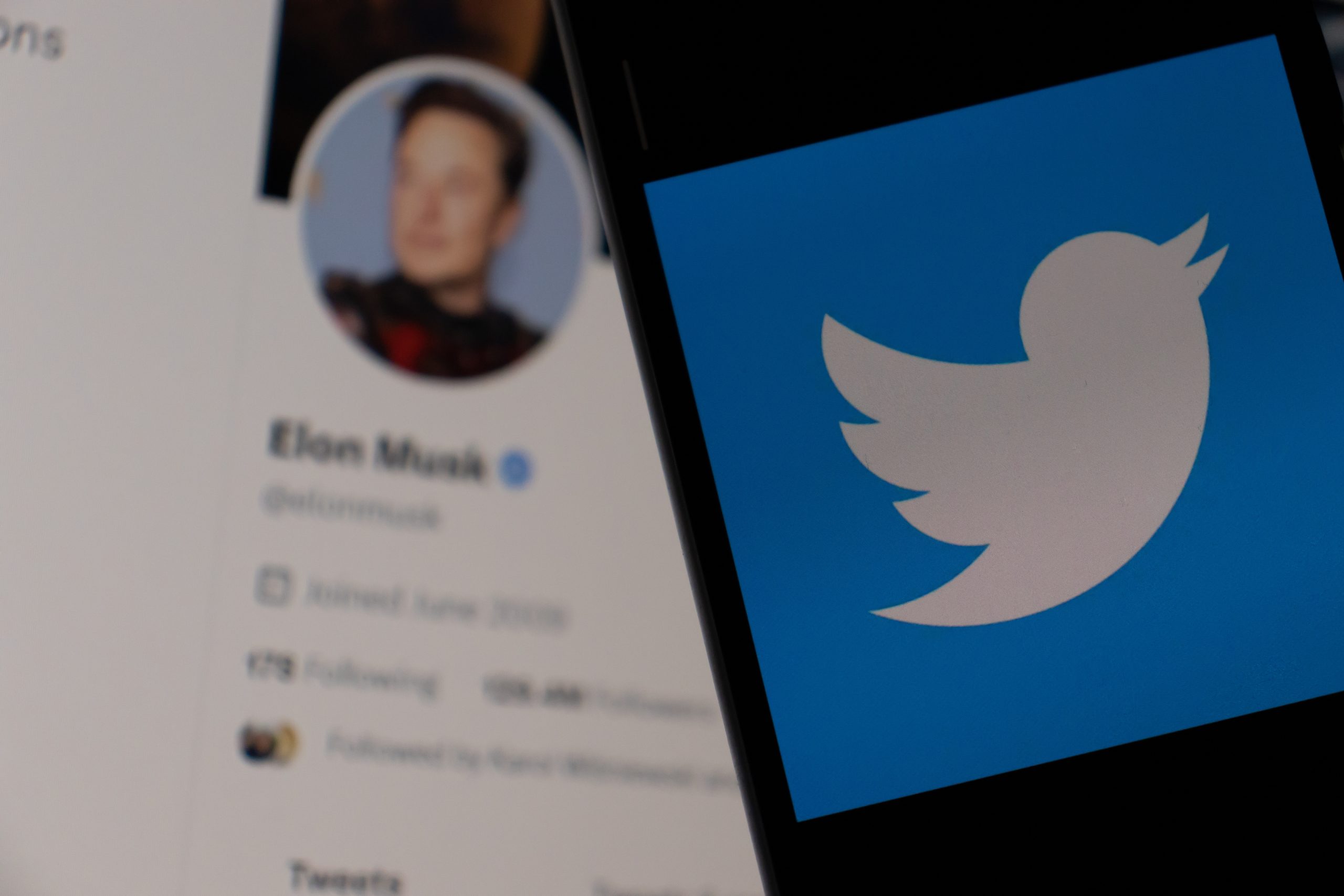 Smartphone with Twitter logo on the screen. Elon Musk on background